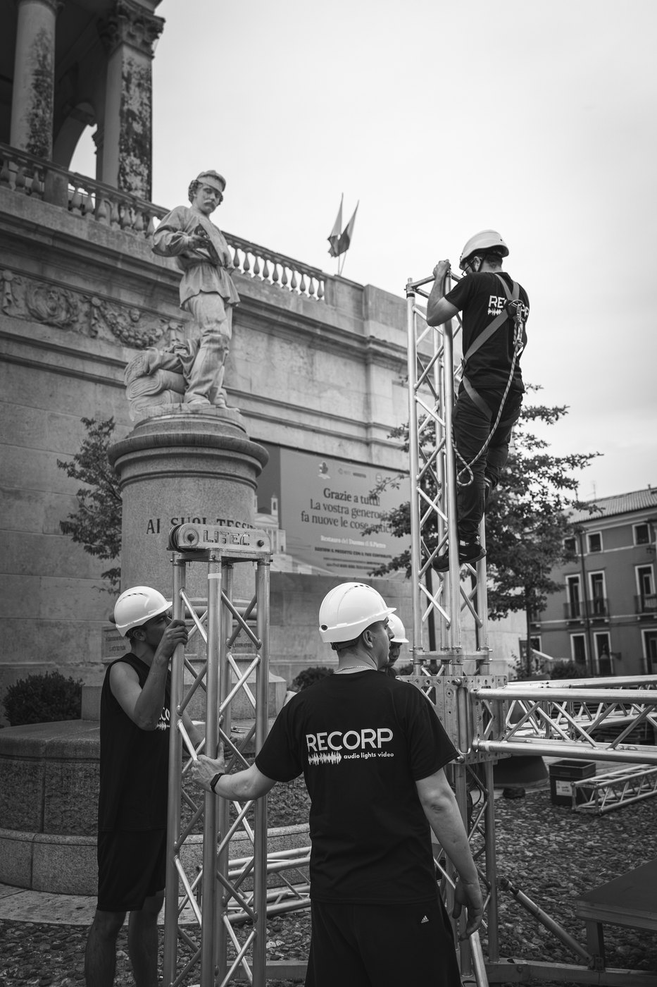 I tecnici con il casco lavorano al montaggio, ripresi di spalle.
